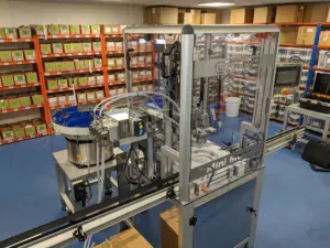 Mini Mono Automatic, Center stage in a production environment, surround by product the machine has filled and capped.